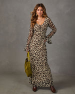 Woman in a sheer leopard print maxi dress with flared sleeves, holding an olive suede hobo bag, styled with brown ankle boots