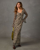 Woman in a sheer leopard print maxi dress with flared sleeves, gold necklaces, olive suede bag and brown ankle boots