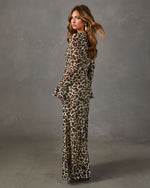 Woman in a sheer leopard print maxi dress with flared bell sleeves and gold earrings, looking over her shoulder
