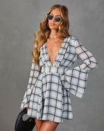 Women's gray plaid mini dress with deep V-neck, bell sleeves, and fit-and-flare silhouette, styled with sunglasses and black woven bag