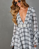 Woman wearing gray plaid deep V-neck dress with bell sleeves, layered gold necklaces and tinted sunglasses