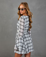 Woman wearing gray plaid long-sleeve mini dress with smocked waist, styled with gold sunglasses and hoop earrings