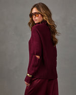 Woman in a burgundy ribbed turtleneck sweater with elbow cutouts and satin midi skirt, wearing tinted aviator sunglasses
