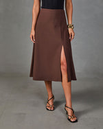 Brown midi A-line skirt with front slit, styled with black strappy heels and gold cuff bracelet, worn with black ribbed top