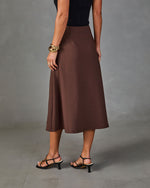 Brown midi A-line skirt styled with black ribbed top, strappy heels, and gold bangles, back view