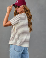 Woman wearing cream striped t-shirt with burgundy stripes, LA baseball cap, sunglasses, and light blue jeans, back view