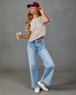Woman in striped crop tee, wide-leg light wash jeans, white sneakers, and burgundy baseball cap holding iced coffee