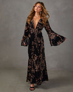 Black velvet floral maxi dress with deep V-neck, knotted waist and flared bell sleeves, styled with gold jewelry and clutch