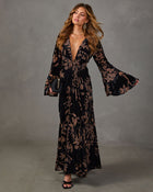 Black velvet floral maxi dress with deep V-neck, knotted waist and flared bell sleeves, styled with gold jewelry and clutch