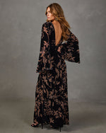 Woman in black velvet maxi dress with tan floral print, open back and bell sleeves, paired with black heeled sandals