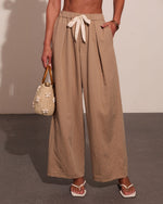 Woman wearing beige linen wide-leg pants with tie waist and pockets, holding woven straw handbag, white sandals