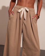 Woman wearing beige linen wide-leg pants with drawstring tie and side pockets, gold bracelets on wrist