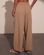 Woman wearing beige linen wide-leg pants with elastic waistband and pockets, styled with gold bracelets and sandals