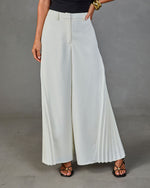 Wide-leg cream pleated trousers with high waist and belt loops, styled with black strappy heels and gold bracelet