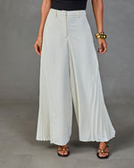 White wide-leg pleated palazzo pants with high waist, worn with black strappy sandals and gold cuff bracelet