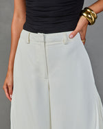 White wide-leg trousers with belt loops, paired with black ruched top and gold cuff bracelet on woman