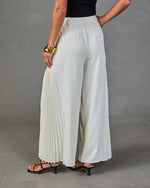 Wide-leg pleated ivory trousers with tailored waistband, styled with black kitten heel sandals and gold cuff bracelet