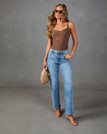 Woman wearing brown cami bodysuit, light wash wide-leg jeans, nude strappy heels, aviator sunglasses, holding woven clutch