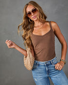 Woman wearing brown tank top bodysuit, blue jeans, woven beige bag, gold jewelry, and aviator sunglasses