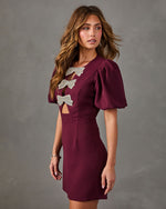 Burgundy mini dress with puff sleeves, cutout bodice and three crystal rhinestone bow embellishments, styled with gold jewelry