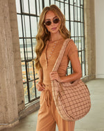 Woman wearing tan ribbed henley bodysuit and drawstring joggers carrying a quilted puffer crossbody tote bag in blush beige