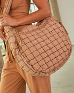 Quilted puffer crossbody bag in dusty rose, grid-stitched nylon with drawstring detail, styled with neutral athleisure outfit