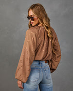 A woman wearing a brown long-sleeve blouse with a subtle tonal pattern and blue jeans, photographed from the back against a textured gray studio background.