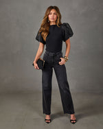 Woman in black puff organza sleeve top, faded black wide-leg jeans, black heels, gold cuff bracelets and black clutch