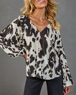 Women's cream and brown cow print oversized blouse with V-neck, balloon sleeves, paired with dark jeans