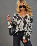 Woman wearing cow print blouse with balloon sleeves, dark jeans, aviator sunglasses, holding black woven leather bag