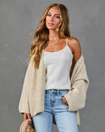 Woman wearing cream oversized knit cardigan, white satin cami, light wash high-rise jeans, holding woven bag