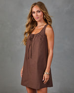 Brown gingham mini dress with tie neckline and A-line silhouette, styled with gold jewelry on female model
