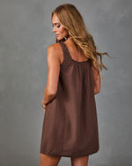 Woman modeling brown plaid sleeveless mini shift dress with A-line silhouette, viewed from back, neutral gray background