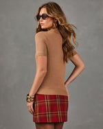 A woman photographed from the back wearing a fitted short-sleeve tan top and a red plaid mini skirt, posed against a plain gray studio background.