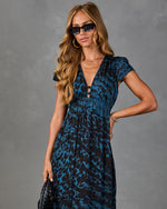 Woman wearing blue leopard print midi dress with deep V-neck, cap sleeves, empire waist, styled with gold jewelry and sunglasses