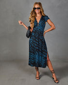 Woman wearing teal blue leopard print midi dress with V-neck, cap sleeves, side slit, styled with black strappy heels and clutch