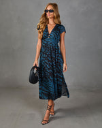 Woman wearing blue black leopard print midi dress with V-neck, cap sleeves, strappy heels, and black woven bag