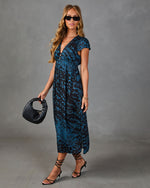 Woman wearing blue leopard print midi dress with deep V-neck, black strappy heels, woven bag, and sunglasses