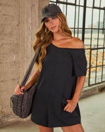 Woman wearing black off-shoulder mini dress with pockets, quilted shoulder bag, and LA baseball cap in urban setting