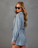 Woman modeling slate blue long-sleeve shirt dress with drawstring waist, sunglasses, and gold hoop earrings, side view