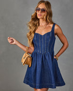 Woman wearing dark blue denim mini dress with corset bodice, aviator sunglasses, tan bag, and gold jewelry