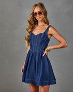 Dark wash denim corset mini dress with sweetheart neckline and flared skirt, styled with gold jewelry and sunglasses