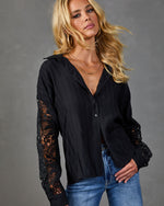 Black lace-sleeve button-down blouse on blonde model paired with blue jeans and layered gold necklaces