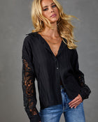 Black lace-sleeve button-down blouse on blonde model paired with blue jeans and layered gold necklaces