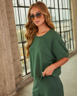 Woman wearing forest green cropped sweatshirt and matching wide-leg pants set, styled with gold hoop earrings and aviator sunglasses