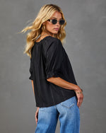 Woman wearing black striped puff-sleeve blouse with blue jeans, gold accessories, and round sunglasses, back view