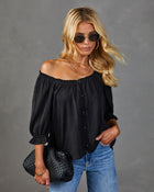 Black off-shoulder blouse with button front and ruffle sleeves styled with blue jeans and woven black clutch bag