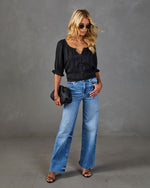 Woman wearing black ruffle blouse, wide-leg light wash jeans, black heeled sandals, holding woven clutch, with sunglasses