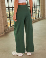 Woman wearing forest green wide-leg high-waist sweatpants with back pocket and decorative seams, paired with white chunky sneakers
