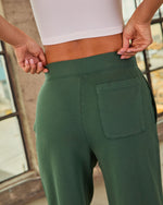 Woman wearing forest green high-waist wide-leg sweatpants with back patch pocket and white crop top, rear view